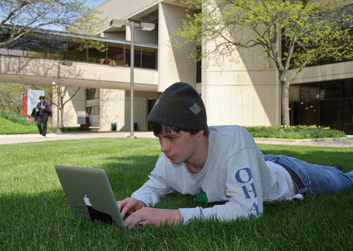 student on campus lawn with laptop